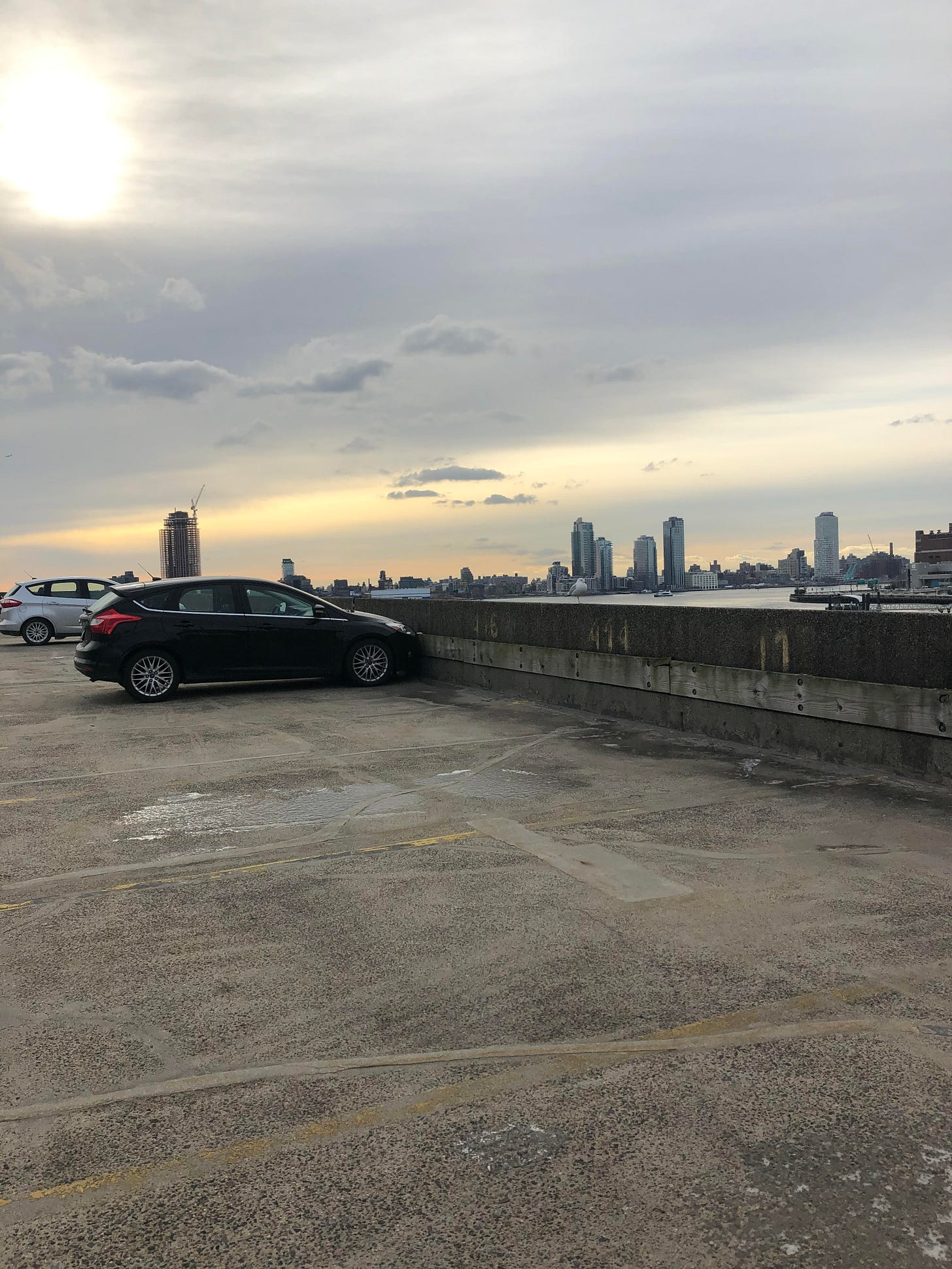 Sara's black Ford Focus parked on an open garage rooftop along the East River at sunset, with a view of Queens under a slightly cloudy sky. Sara's black Ford Focus parked on an open garage rooftop along the East River at sunset, with a view of Queens under a slightly cloudy sky.