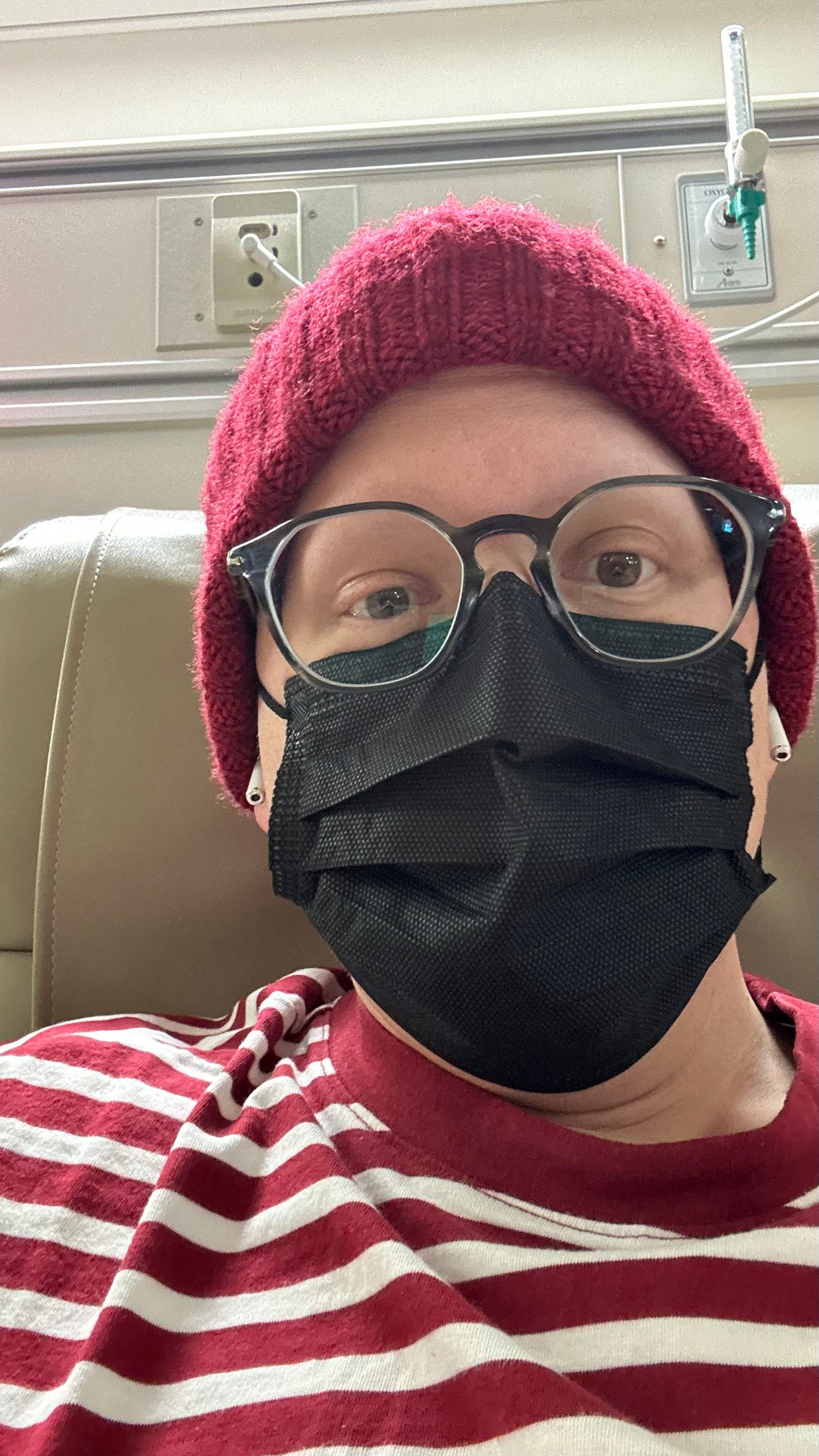 picture of a man wearing a red striped shirt, black face mask, glasses, and red toque in a hospital