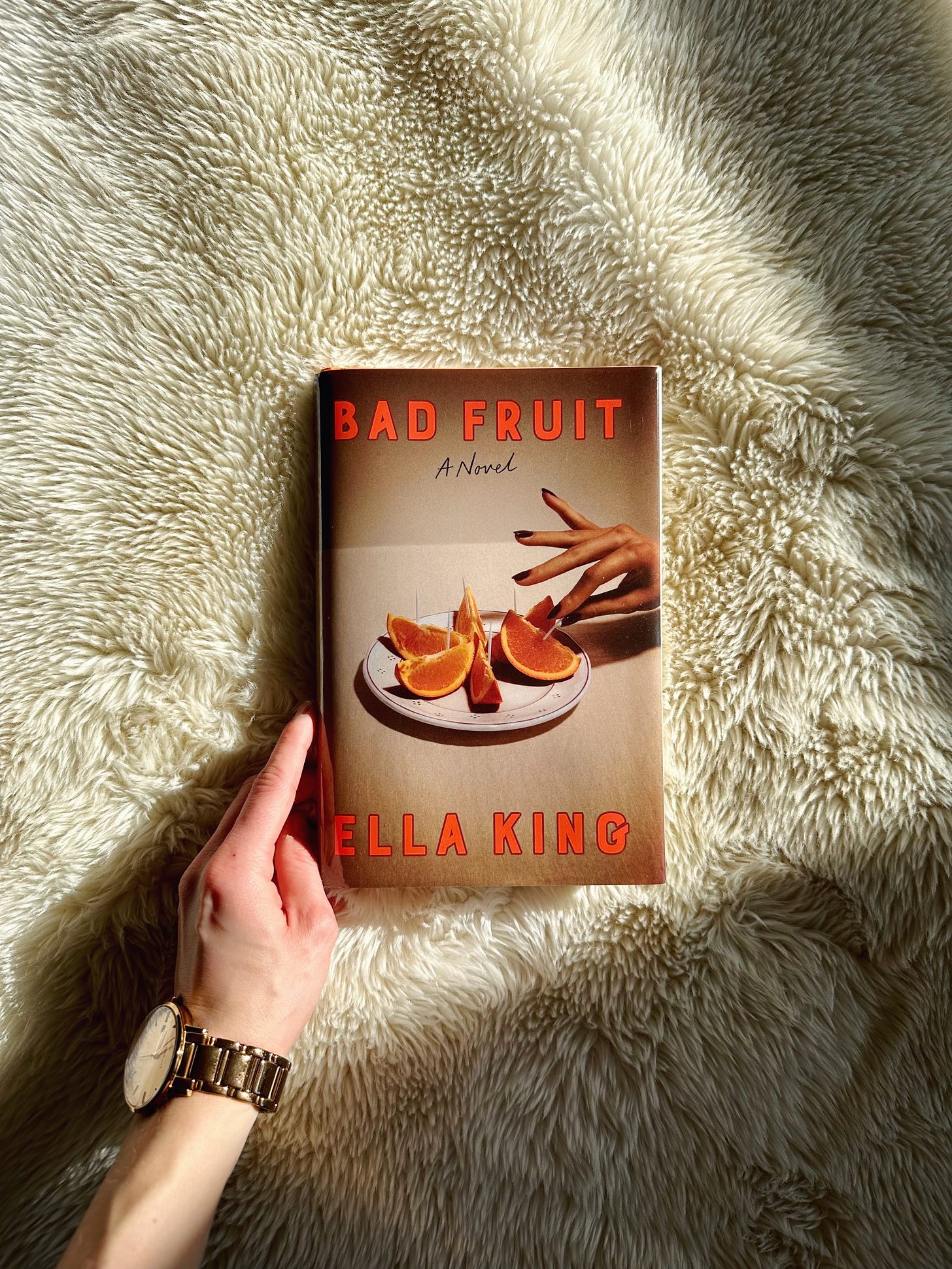 A white hand holds a copy of Bad Fruit against a white blanket, shrouded in shadows