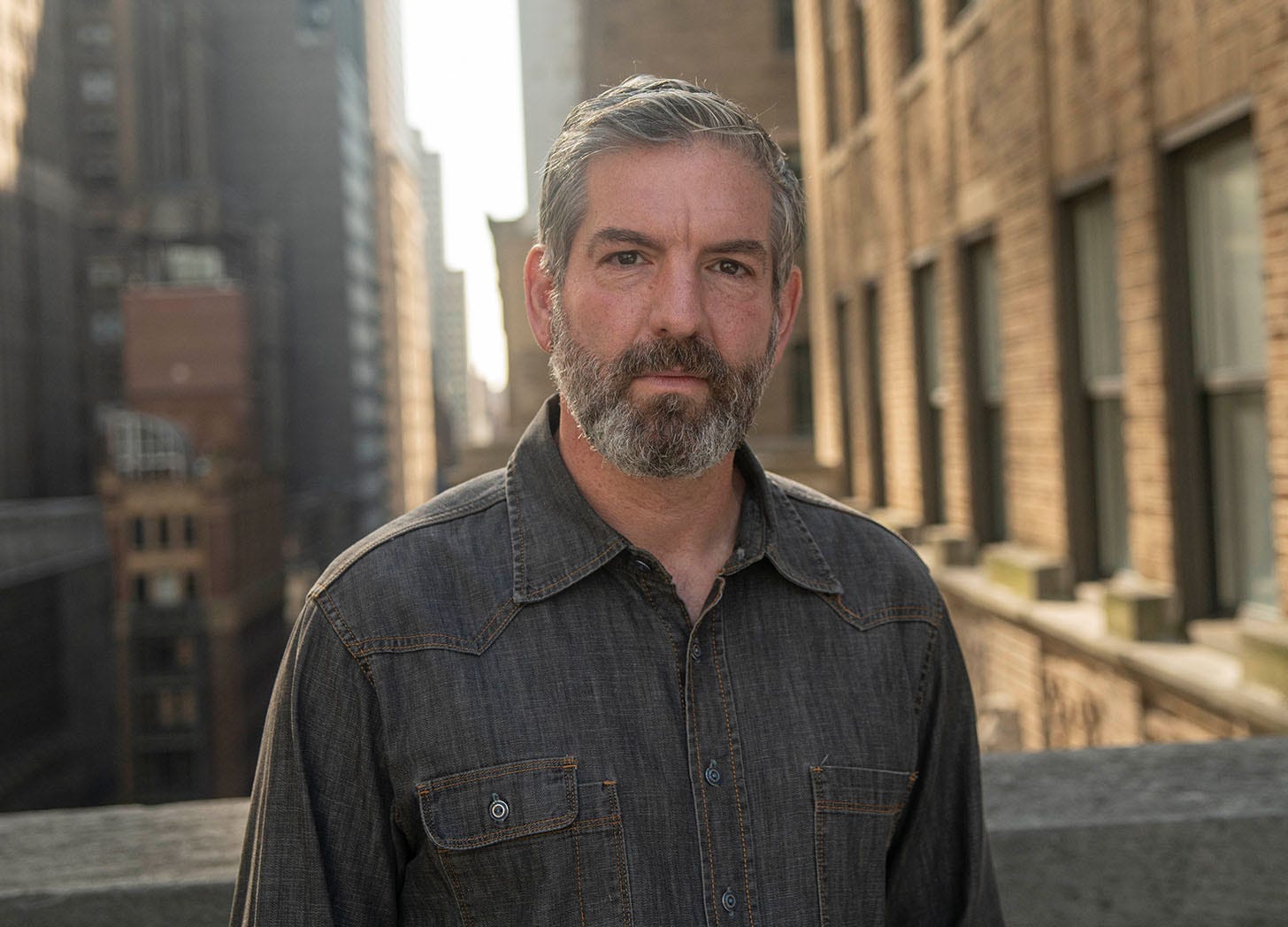 Former Rolling Stone editor-in-chief Noah Schactman stands on a balcony with a blurry cityscape in the background