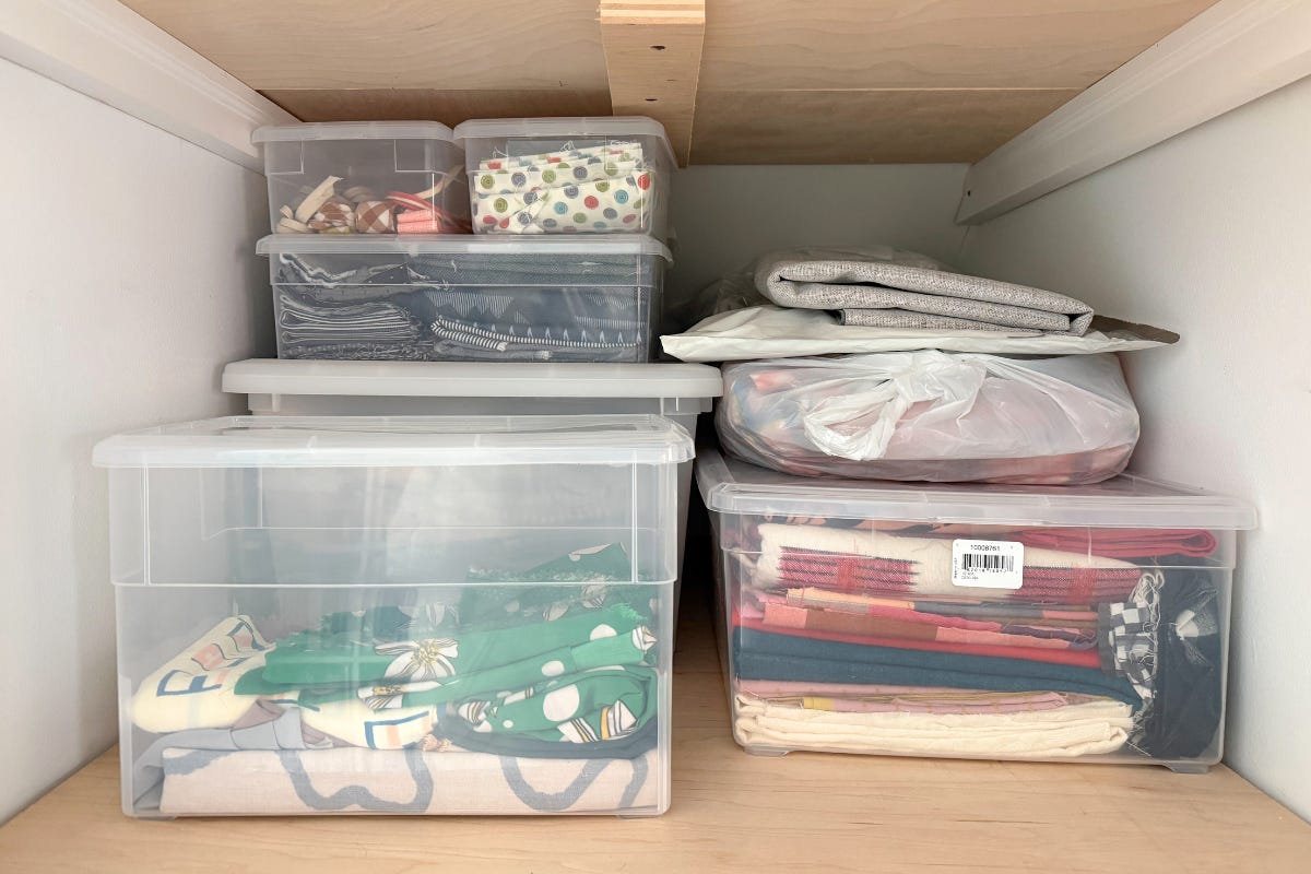 Clear storage bins on wooden shelves containing fabric scraps organized by fabric type
