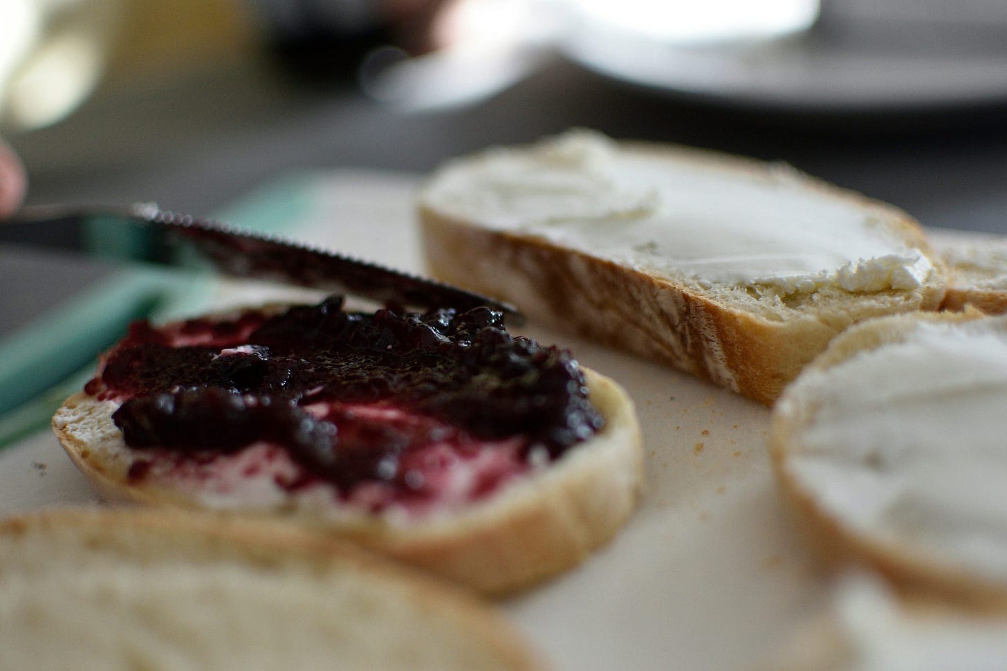 Photograph of a few slices of homemade bread, with butter. A dark red jam is being spread on one of the slices.