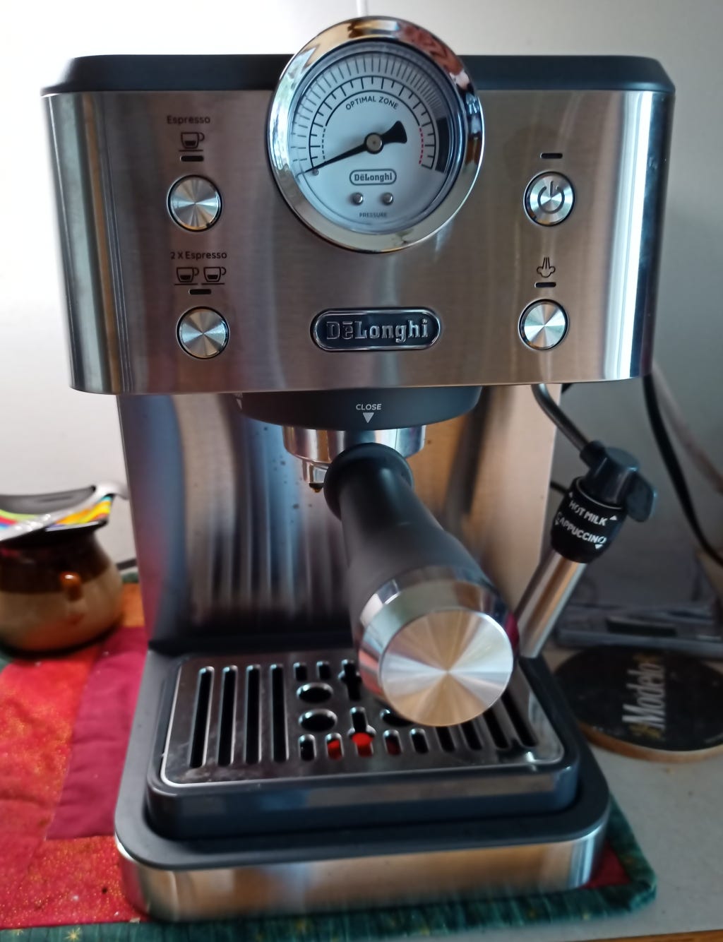 An espresso/cappuccino coffee machine. A Pressure dial dominates the centre of the front panel and is set so that it crowns just above the rest of the machine. there are four circular crome buttons, each with a LED indicator above and icons to indicate single and double cup espressos (on the left), and power /steam on the right.