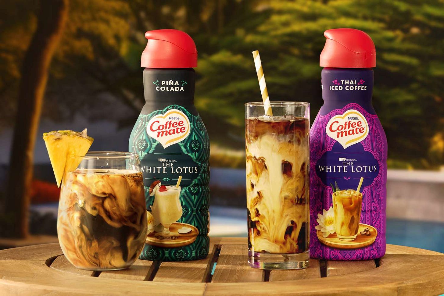 Coffee mate® THE WHITE LOTUS® Pina Colada Flavored Creamer and Thai Iced Coffee Flavored Creamer bottles by a pool.