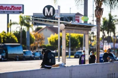 People waiting at a Los Angeles Metro bus stop with black and white M logo.