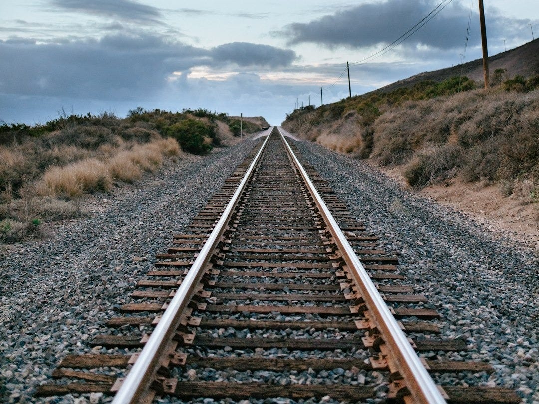 gray metal train rail under white clouds during daytime gray metal train rail under white clouds during daytime