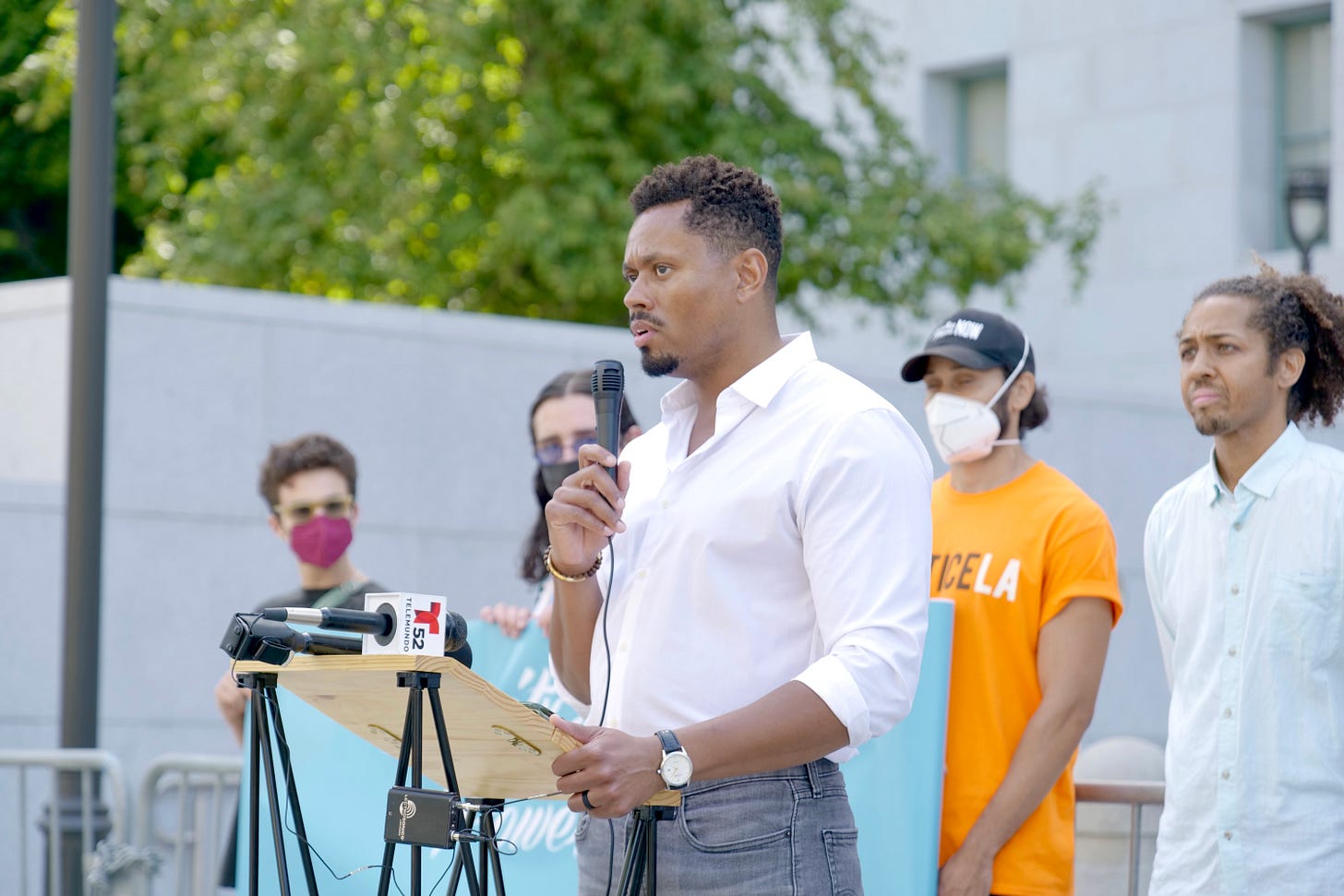 A man standing behind a podium speaks into a microphone as several people stand behind him.