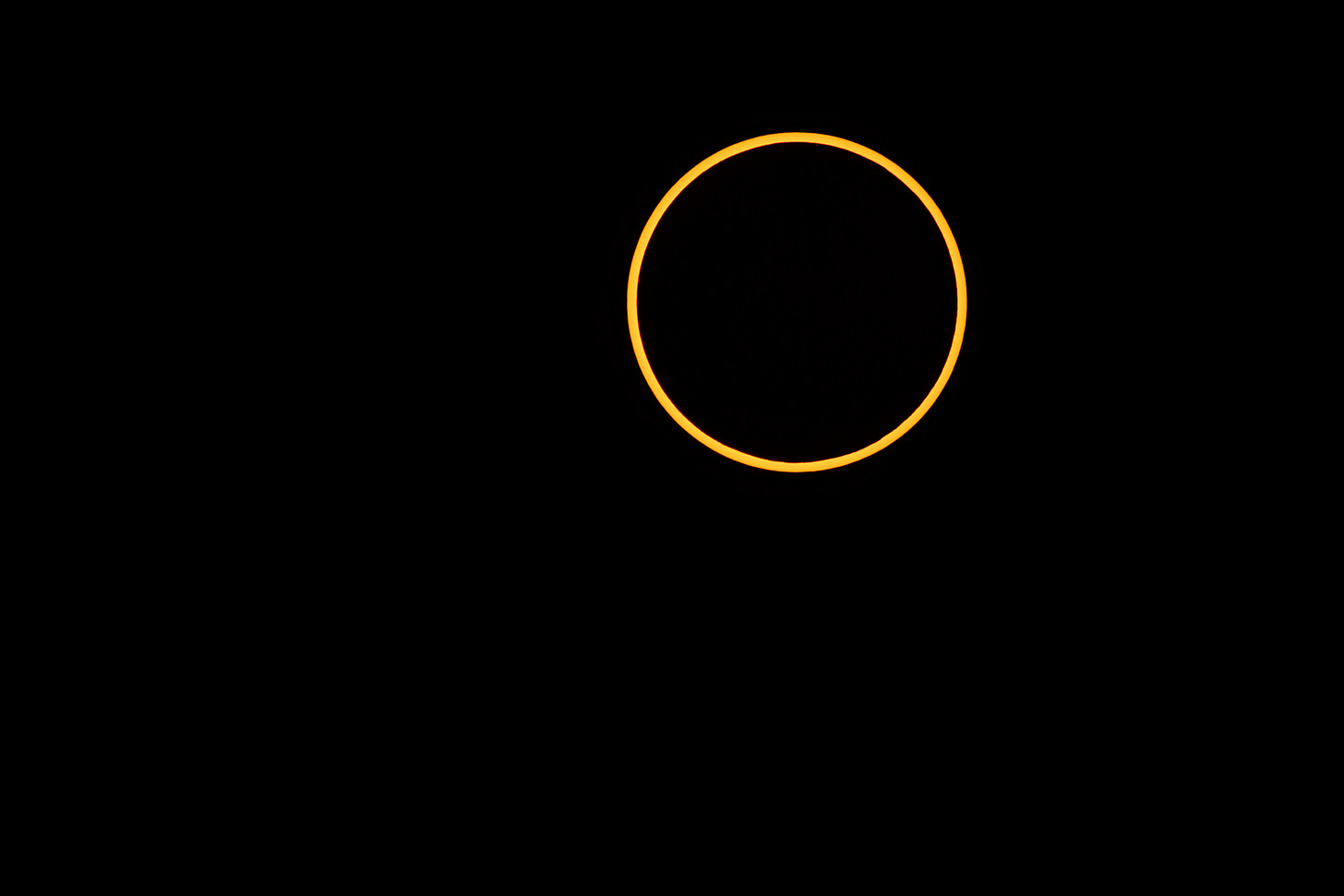 A thin orange ring of sunlight surrounds the dark Moon against a black sky. A thin orange ring of sunlight surrounds the dark Moon against a black sky.