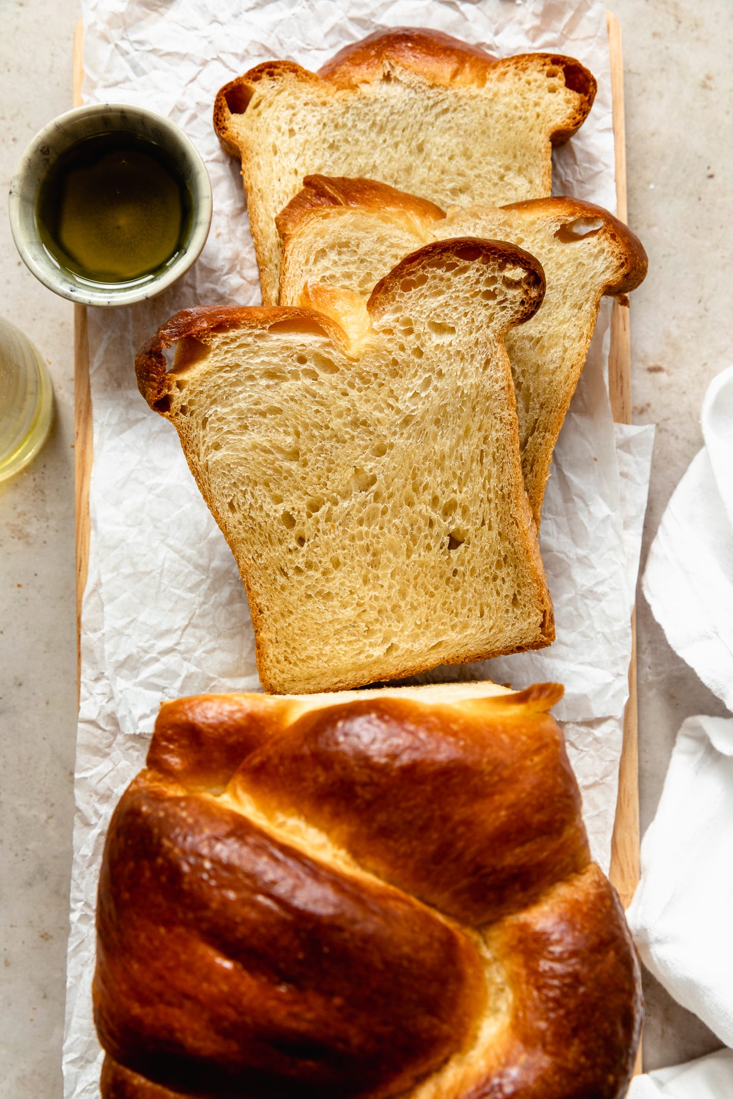 Vegan olive oil brioche slices on parchment on a wooden board on a tan counter