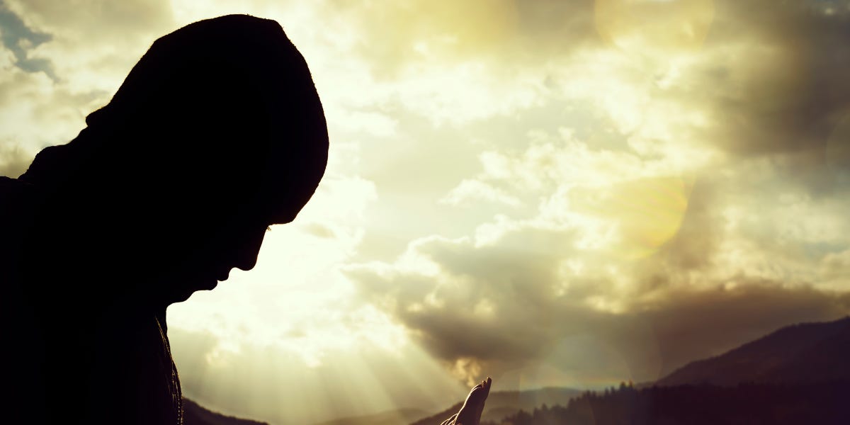 Silhouette of a man praying or in contemplation under a glowing sky – symbolic of spiritual transformation and self-discovery through Mars placements