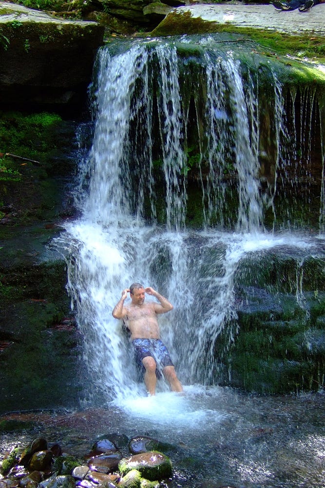 The author leans into the stream of water falling down Buttermilk Falls, taking an impromptu shower