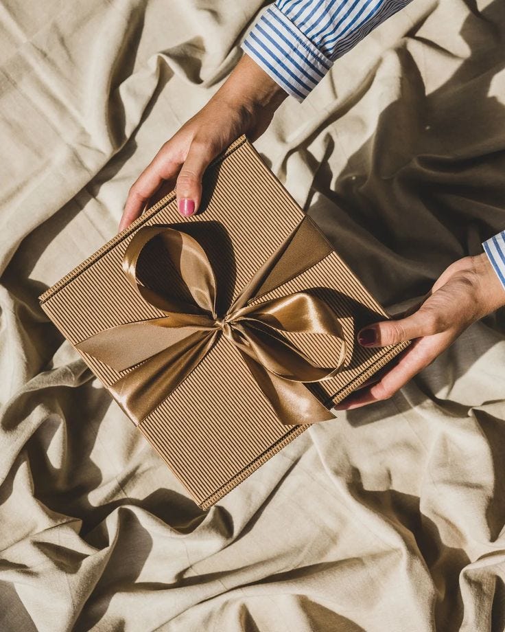 This may contain: a woman's hands holding a brown gift box with a large bow on it