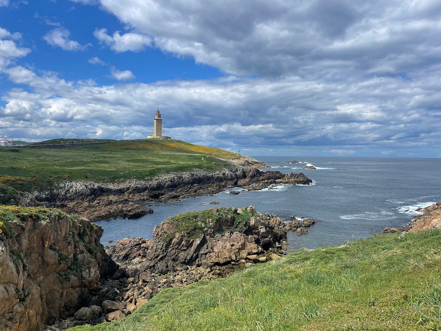 Green cliffs and blue skies over rough seas with a lighthouse in the distance