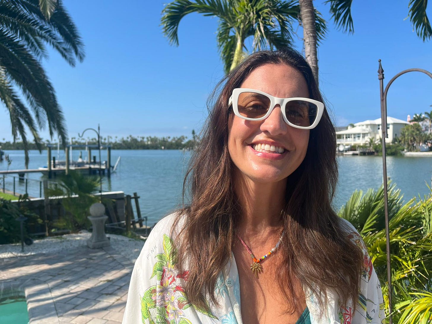 Beauty editor Donna Francis smiling in the Florida sunshine, wearing white sunglasses and a tropical shirt, with a scenic waterfront and palm trees in the background. Beauty editor Donna Francis smiling in the Florida sunshine, wearing white sunglasses and a tropical shirt, with a scenic waterfront and palm trees in the background.