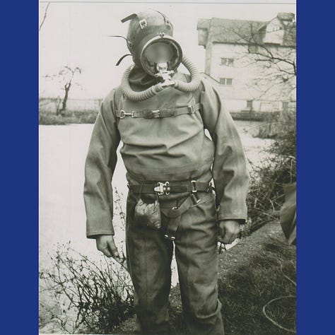 An officer assists a police diver, who is standing in an old style dry suit and full face diving bell helmet with breathing apparatus.
