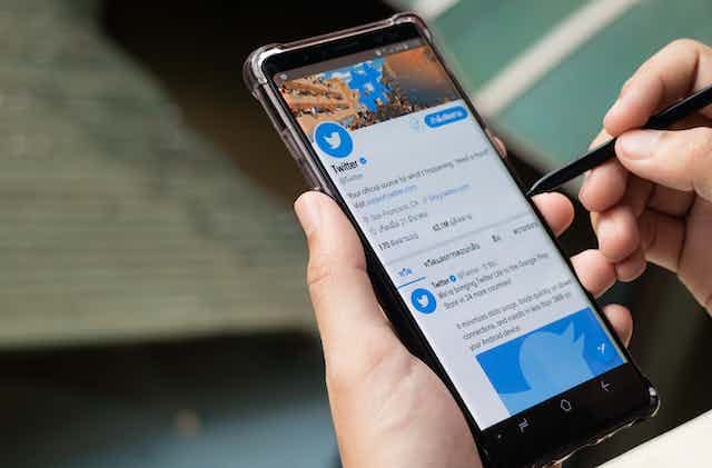 A hand holds a phone showing the Twitter twitter feed A hand holds a phone showing the Twitter twitter feed