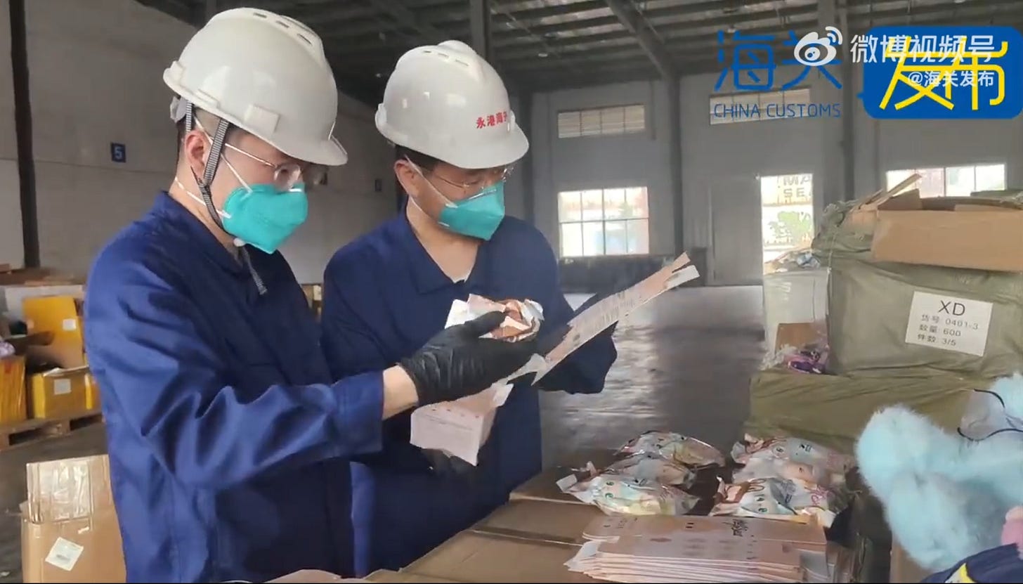 Two helmeted customs officers in blue coveralls examine suspected counterfeit Labubu blind-box packets during a Ningbo warehouse raid. Two helmeted customs officers in blue coveralls examine suspected counterfeit Labubu blind-box packets during a Ningbo warehouse raid.