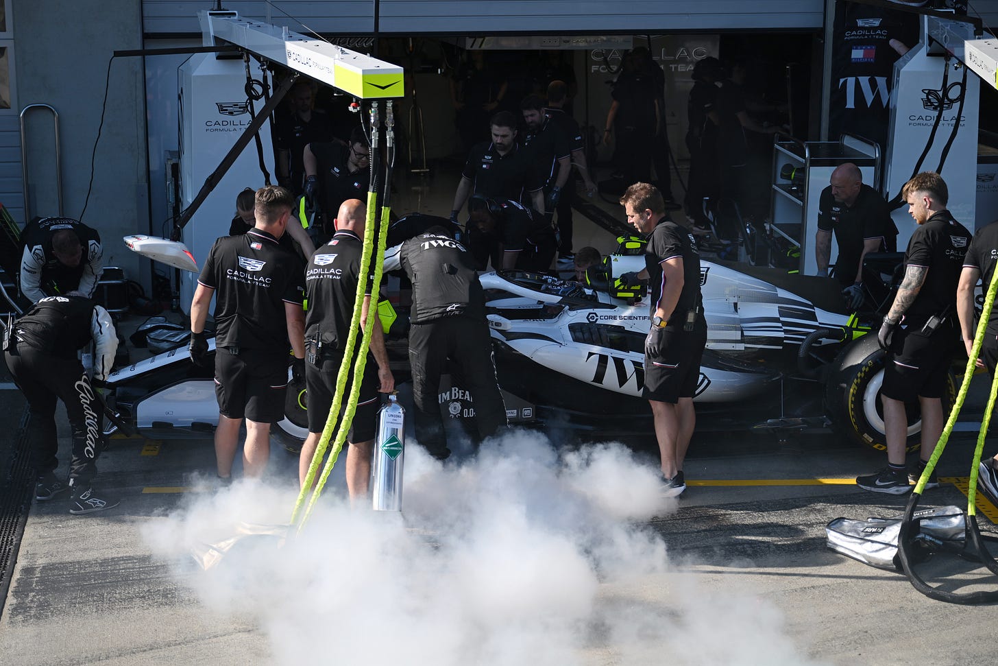 Cadillac mechanics surround the car in the pit box as smoke pours out from underneath the car