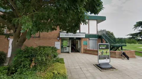 Google Entrance to a building, a golf course is visible in the background, there is a large green tree in the forground