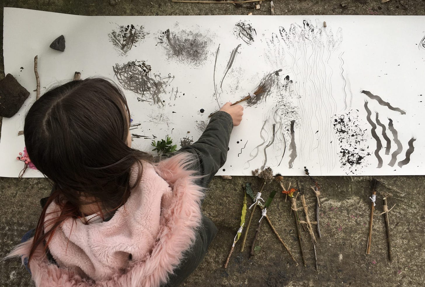 girl making marks on a large piece of paper with charcoal and sticks