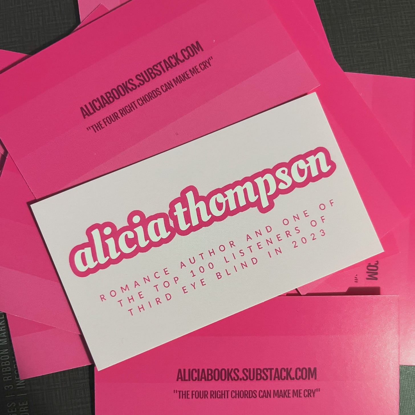 Picture of my Barbie-pink business cards that say "alicia thompson" and then "romance author and one of the top 100 listeners of third eye blind in 2023" on the front and then my substack address and "the four right chords can make me cry" quote on the back