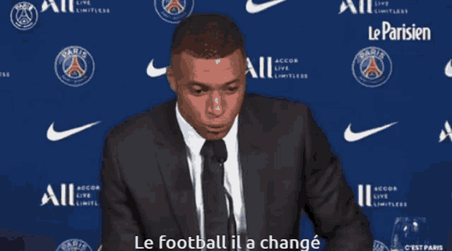 a man in a suit and tie is speaking into a microphone with the words le football il a changé below him