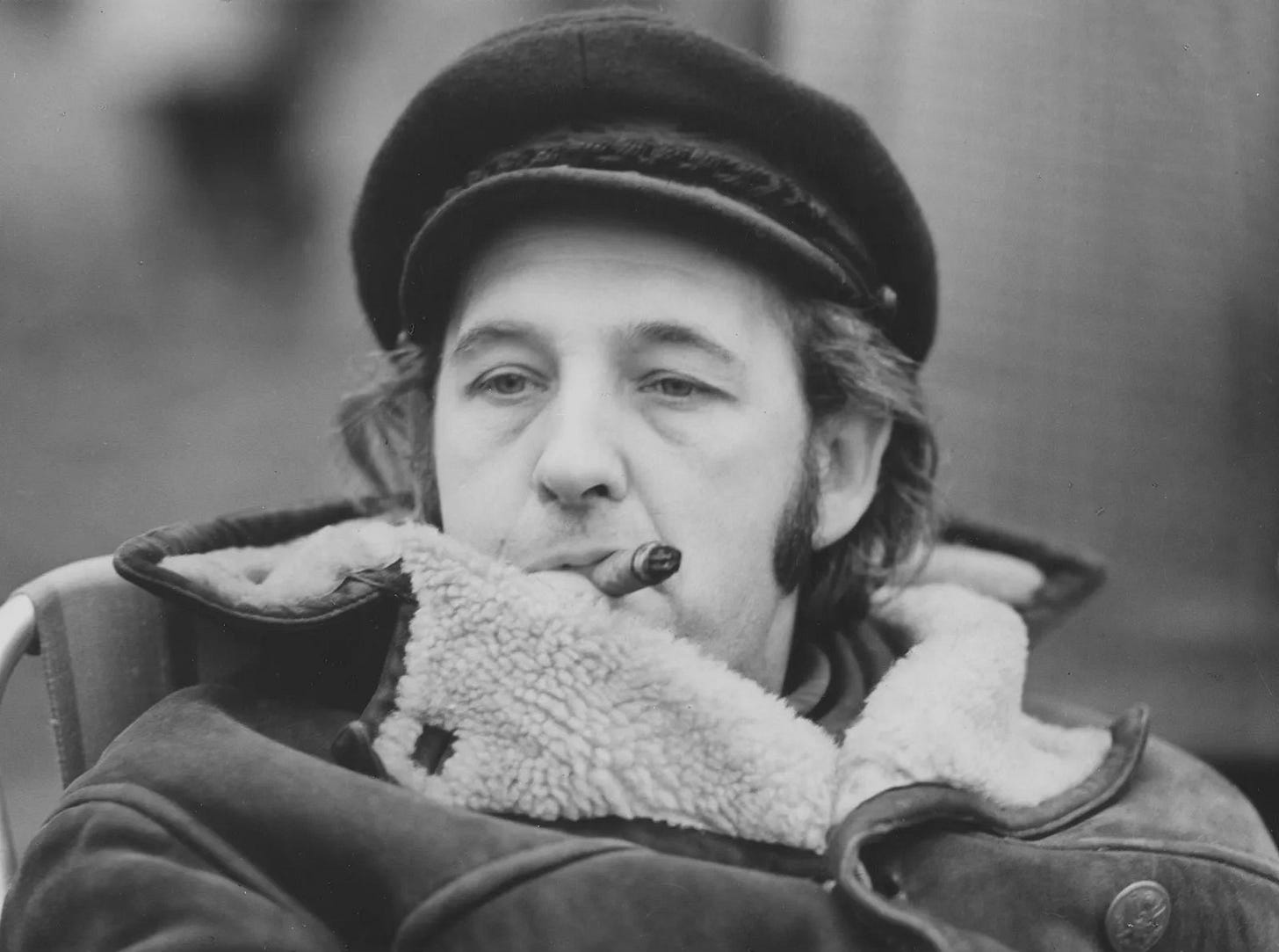 Polish film director Andrzej Wajda, wearing a thick fleecy coat and cap while smoking a cigar.