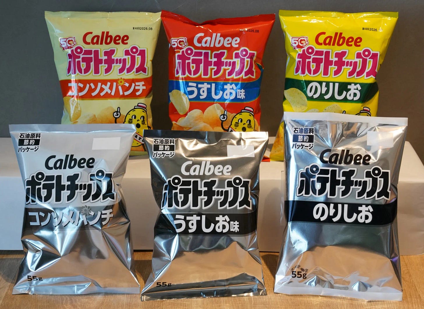 Bags of Calbee potato crisps, sample packages with a black-and-white design (bottom) and the current orange and yellow packaging (upper), are displayed at the company's headquarters in Tokyo on May 14, 2026. Japan's leading potato chip maker is feeling the crunch from shortages related to the Iran war and is swapping its signature orange-and-yellow packets for black and white, reports said. (Photo by Kazuhiro NOGI / AFP via Getty Images) Photographer: KAZUHIRO NOGI/AFP