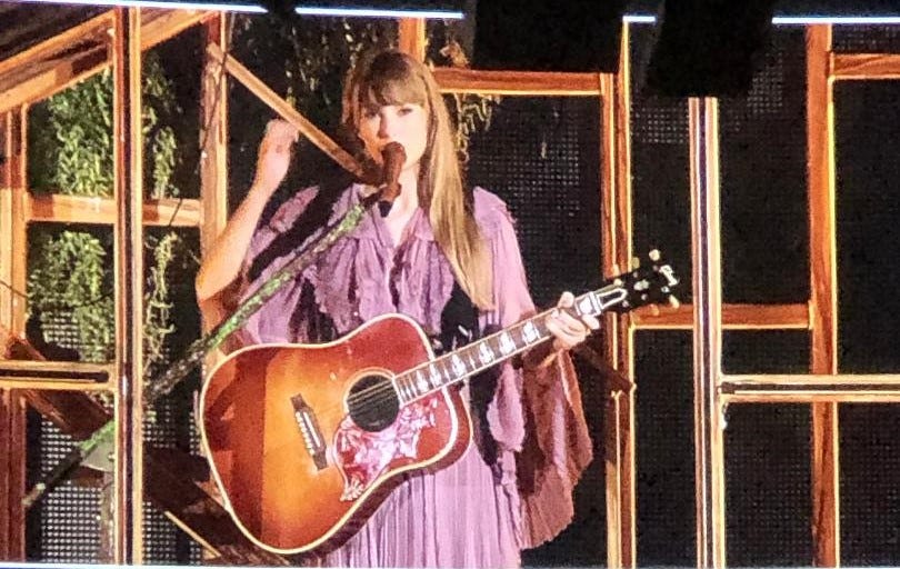 T Swift with acoustic guitar and "Folklore cabin" set, flowing purple dress T Swift with acoustic guitar and "Folklore cabin" set, flowing purple dress