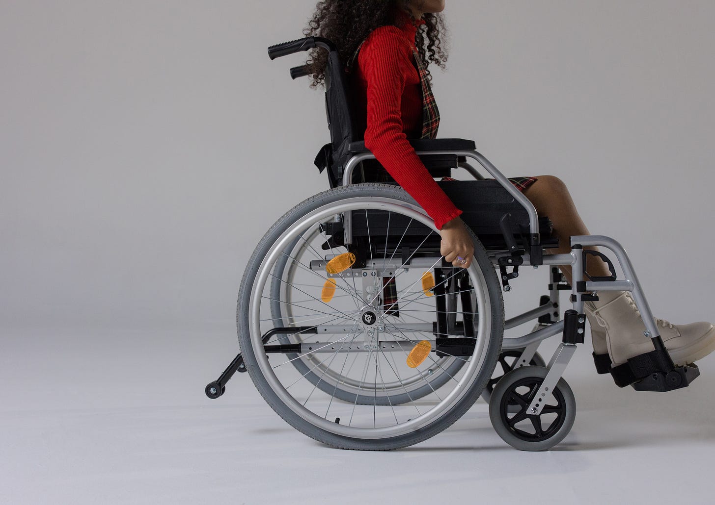 Woman with a red sweater sitting in a manual wheelchair propelling it forward using the back wheels