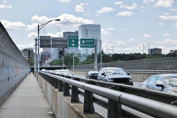 Photo taken from the sidewalk of an unremarkable four-lane highway bridge. Along the left side of the sidewalk there is a chain link fence. Photo taken from the sidewalk of an unremarkable four-lane highway bridge. Along the left side of the sidewalk there is a chain link fence.