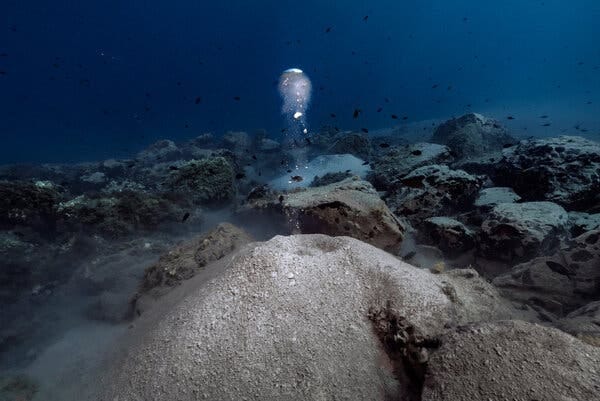Bubbles of gas rise from a collection of underwater rocks. 