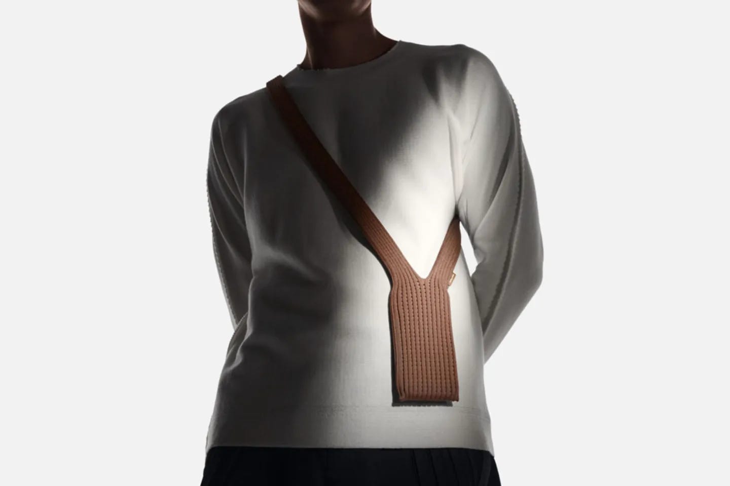A torso in a sweatshirt wearing a tiny knitted bag/pouch that falls just about waist-height that seems to have an iPhone in it