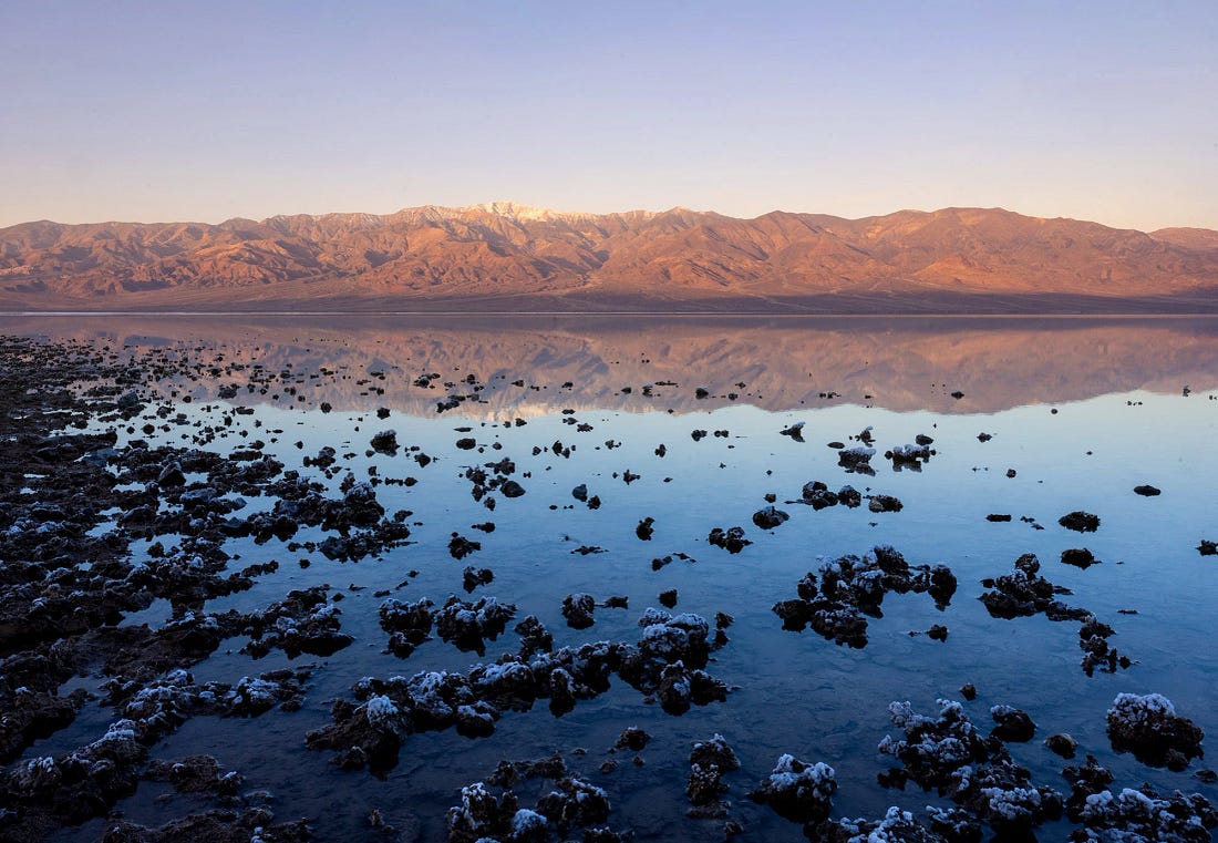 Still water at Lake Manly reflects the Panamint Range and Telescope Peak in Death Valley, with scattered salt formations emerging from the shallow flooded playa. Still water at Lake Manly reflects the Panamint Range and Telescope Peak in Death Valley, with scattered salt formations emerging from the shallow flooded playa.