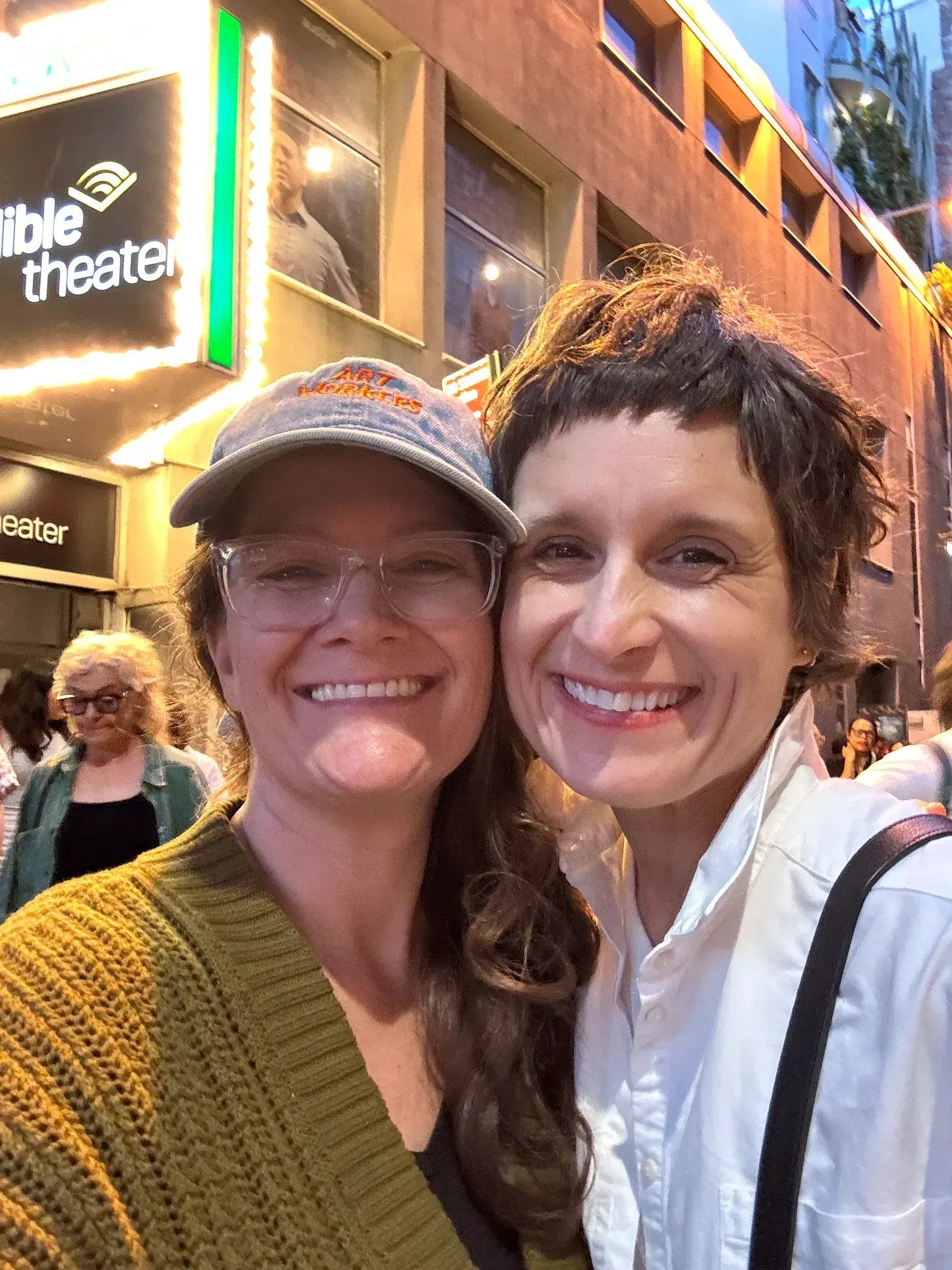  two White friends smiling, cheek to cheek, in front of a marquee. 