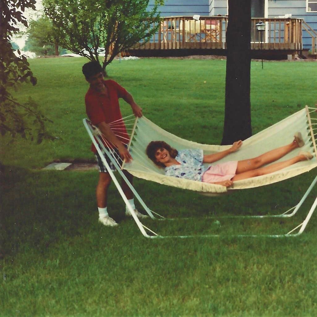 20-something man stands alongside a 20-something woman in a hammock in a backyard 20-something man stands alongside a 20-something woman in a hammock in a backyard