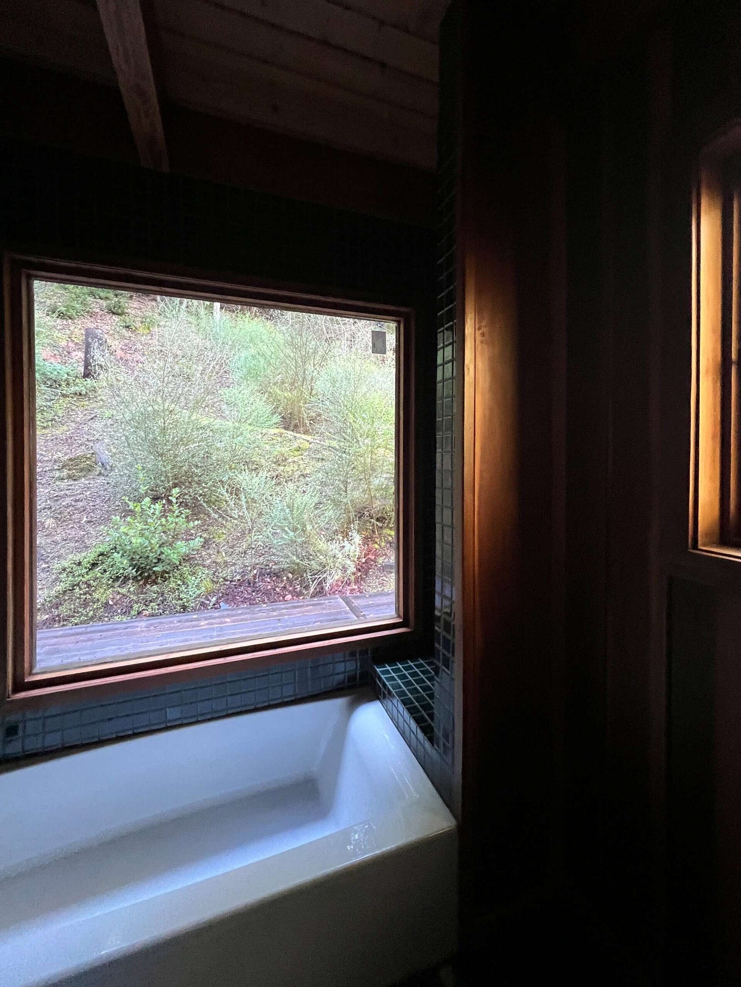 The moody bath with the shiny green tile with the flow of evening light shining onto the tile and white tub.