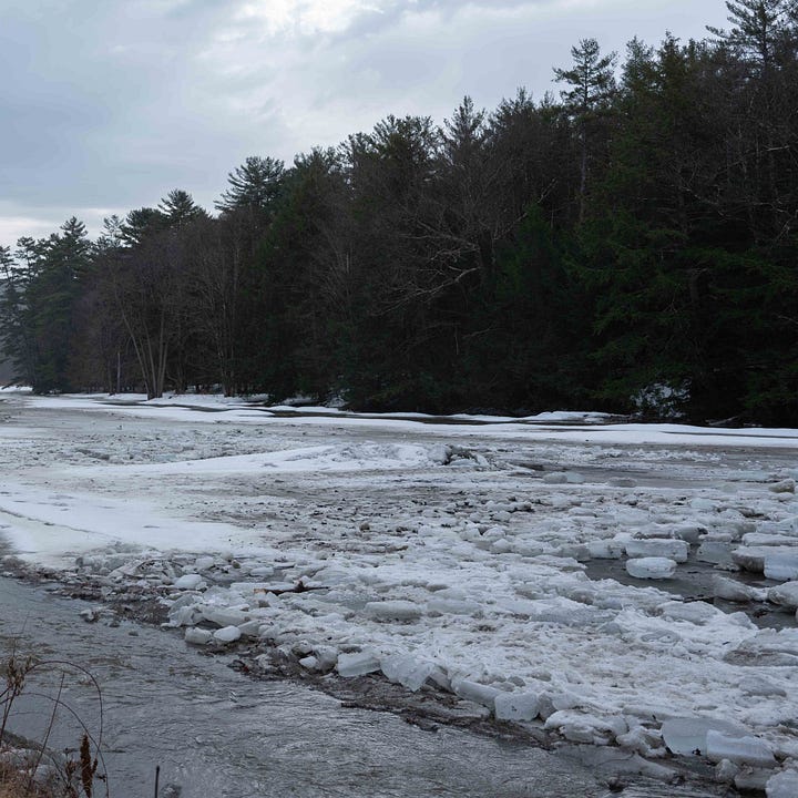 Four photographs of a snow covered rock in the middle of an icy river, which is melting so there is water flowing in the third and forth images.