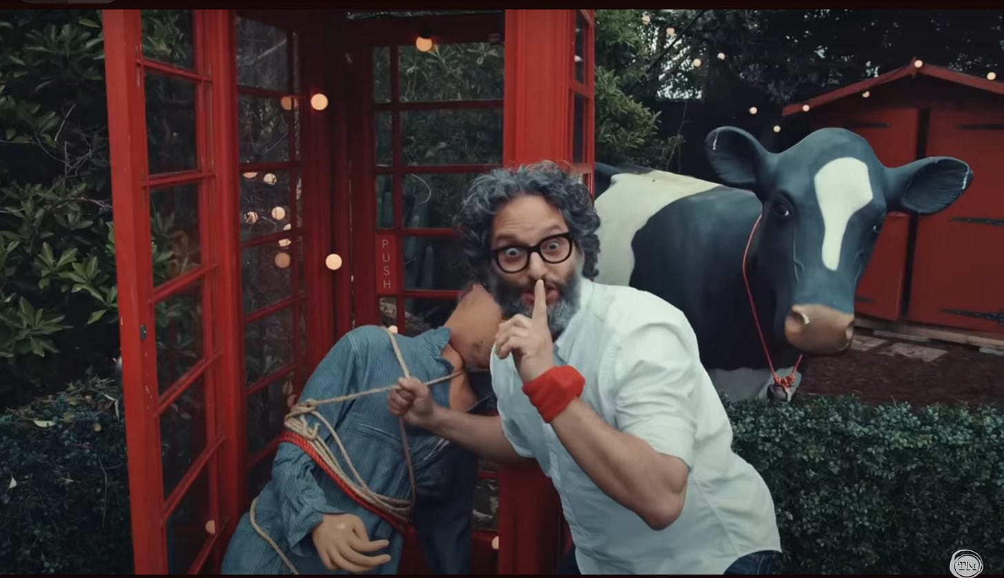 A wide-eyed Jason Mantzoukas, outside a red phone box with a tied-up mannequin, puts his finger to his lips and says, "Shhh!"