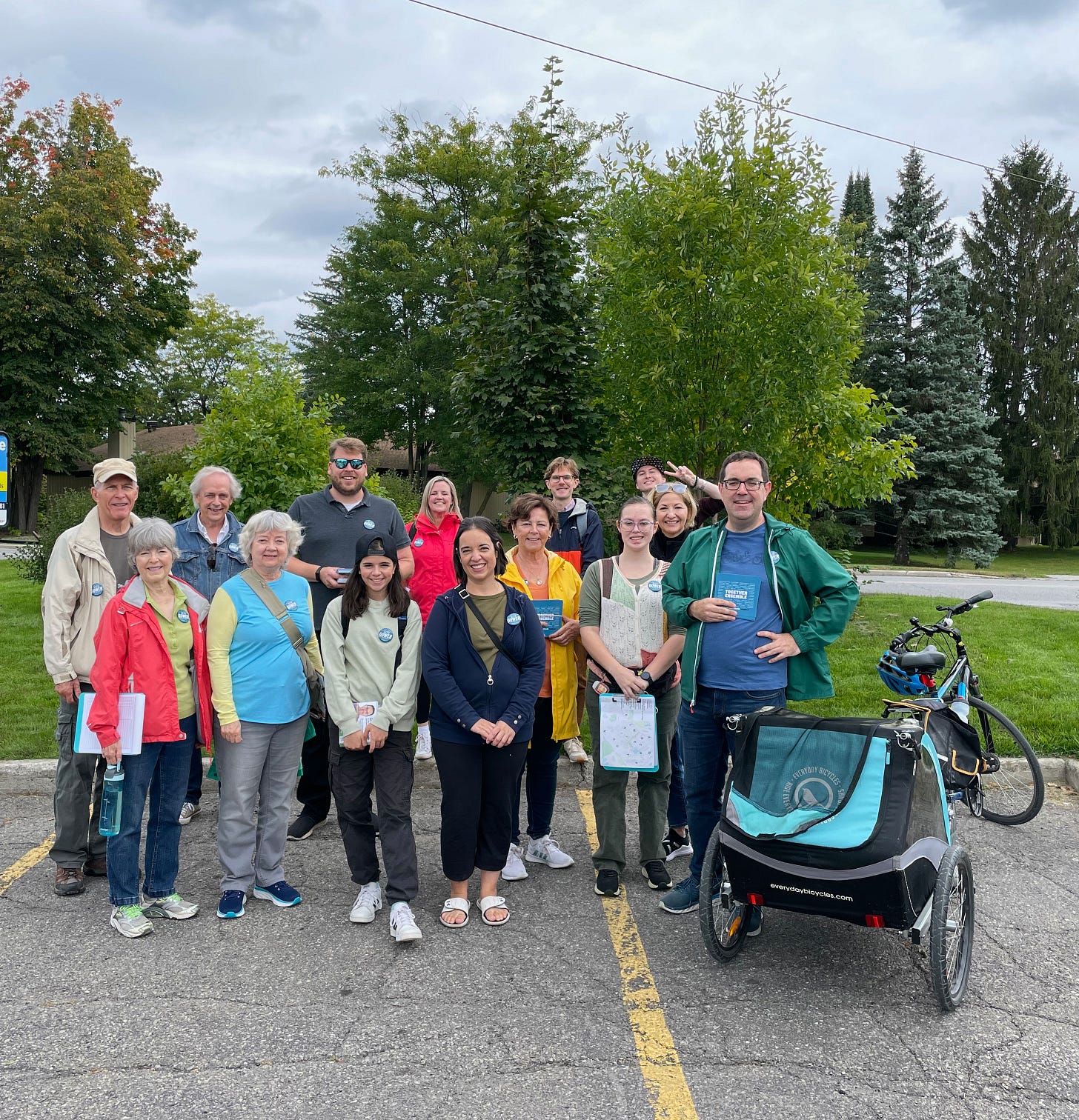 A large group of people standing together, a bike and bike trailer in the foreground