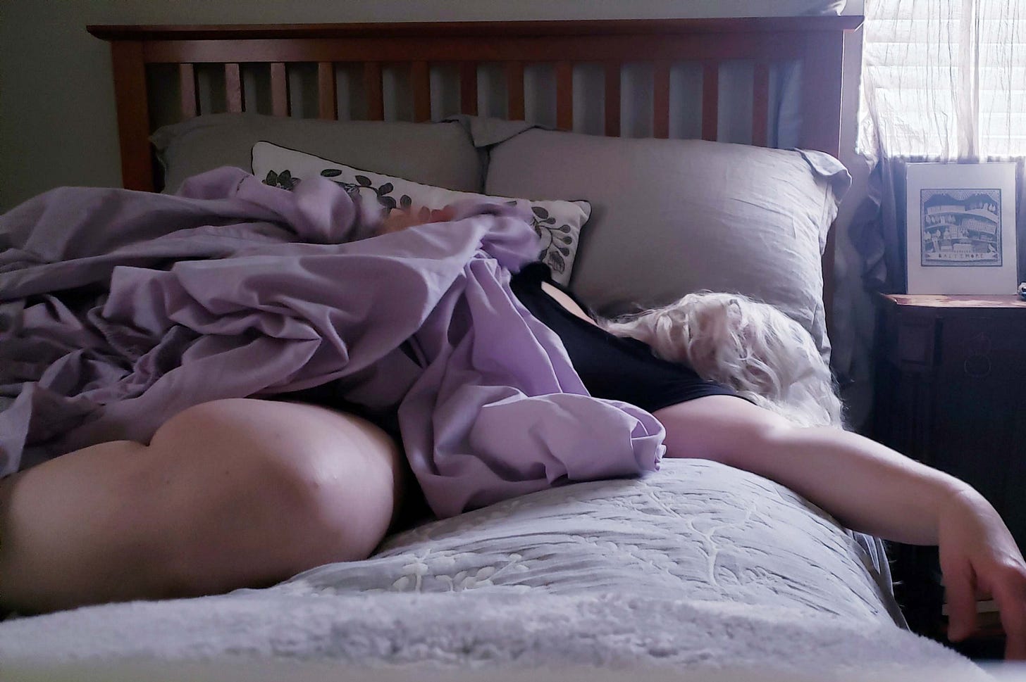 Exhausted woman lying on bed with purple sheets covering her.