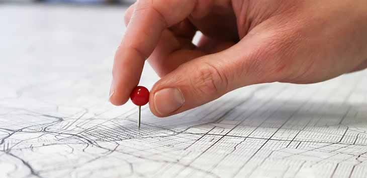 Photo of a hand pushing a pin into a map.