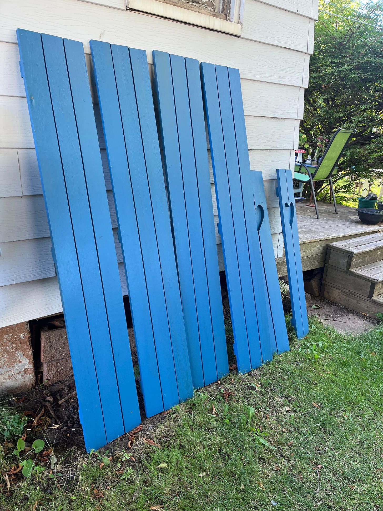 six wooden shutters, painted blue and leanign against the side of my house, waiting to be installed.