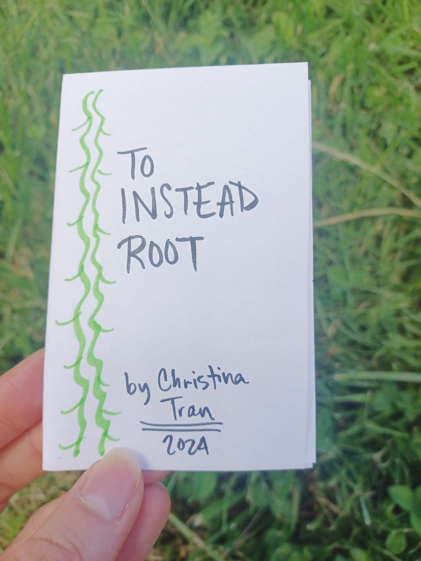 "To Instead Root" -- the cover of a minizine, held against a grassy backdrop