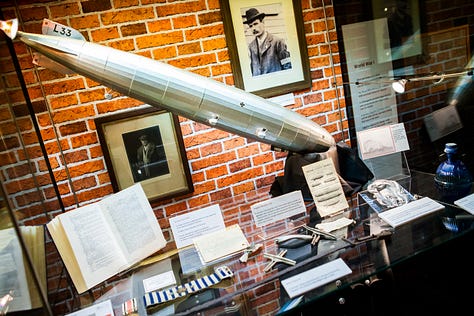 Image one shows the museum display for World War 1, featuring a model zeppelin. Image 2 shows an ornate metal ashtray. A dragon weaves in an out of a horse shoe which circles the entire edge. Top centre the inscription reads made from pieces of Zeppelin L33, Little Wigborough 24.9.16. The third image shows small pieces of the zeppelin's metal framing.