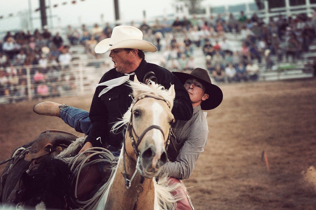 Photograph of a young man helping an older man down from a horse Photograph of a young man helping an older man down from a horse
