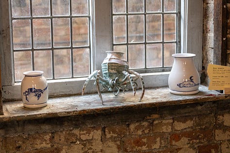 The images show various artworks in a gallery setting. The first is a ceramic pot with crab legs; the second is the word BREAD cut into three doilies; the third is a large, colourful painting of a recumbent Black figure.