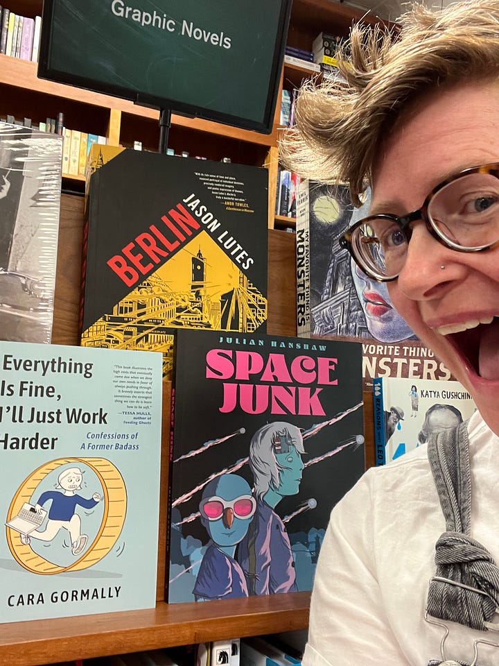 The author with their mouth agape in wonder and delight at their book in the wild in a bookstore; their book on a shelf