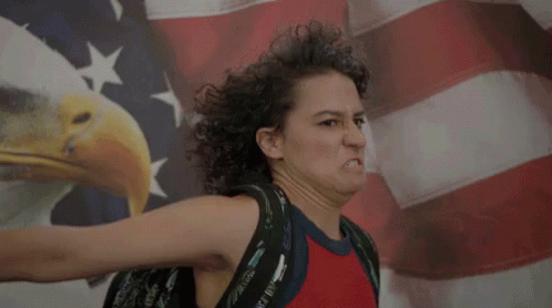 Woman's hair blows back in the wind as she salutes dramatically before a US flag