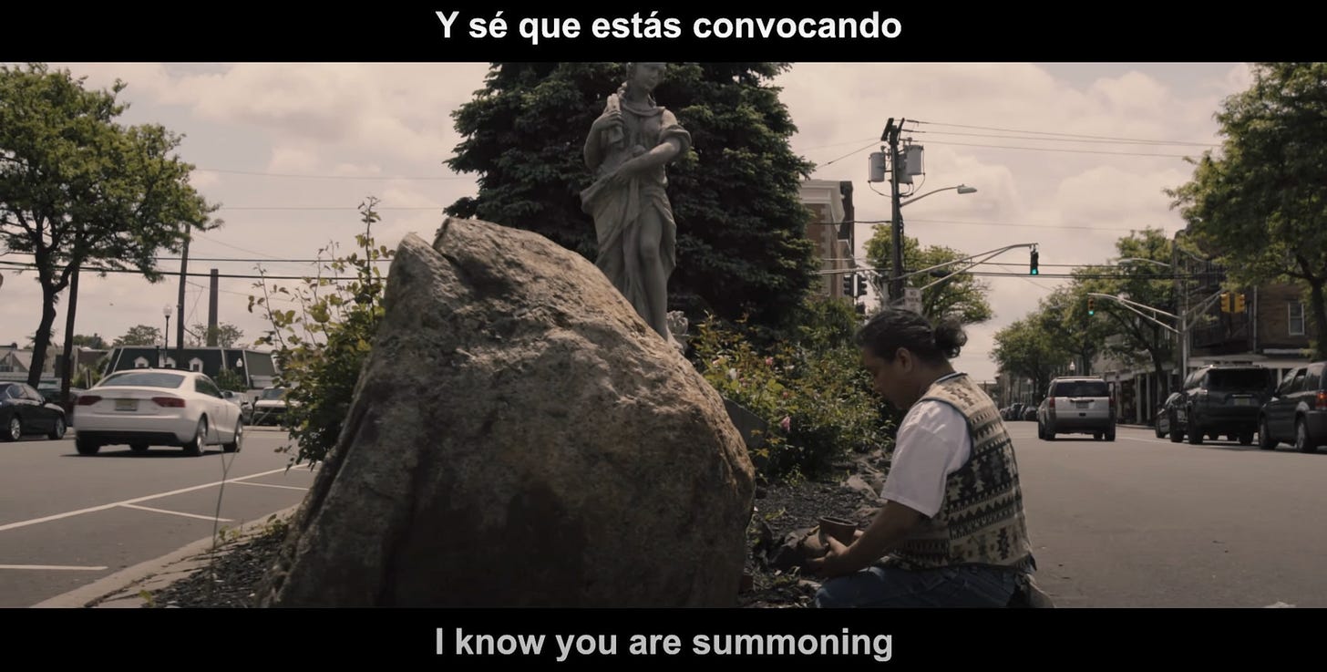 In the island between roads, a healer is kneeling next to a rock, creating an altar-space.